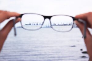 Hands holding glasses up toward a skyline beyond a body of water